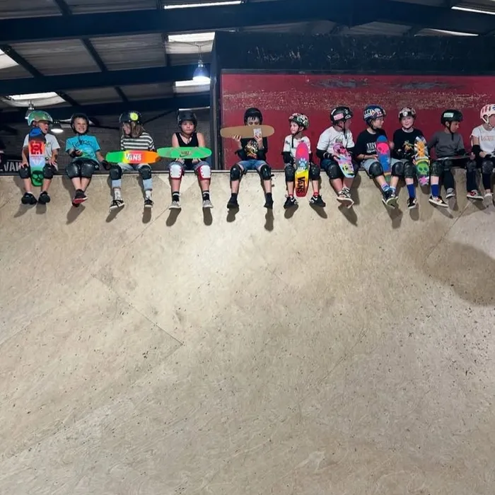 A row of kids in helmets and pads sitting at the top of the ramp at Prevail Skatehouse