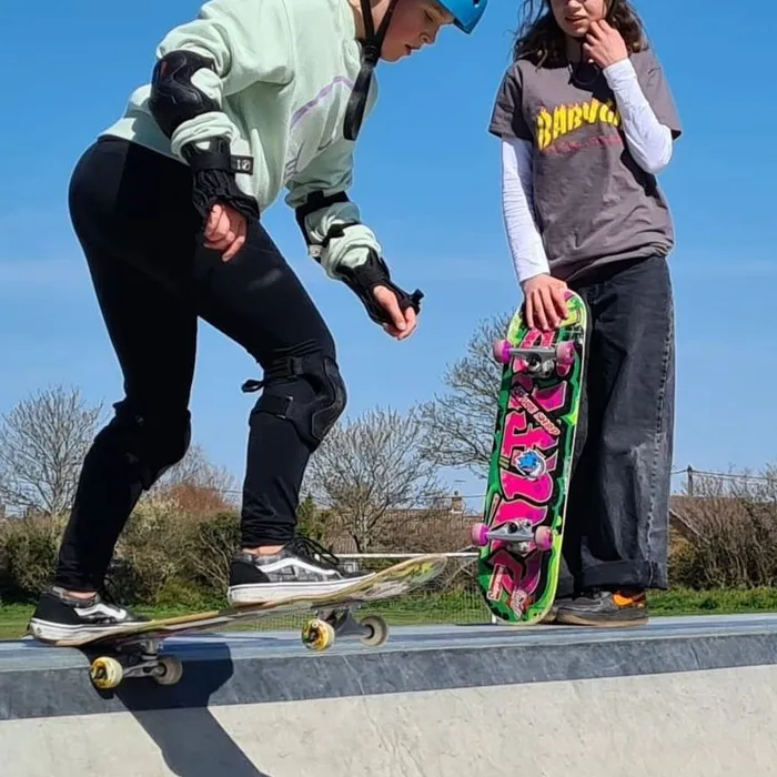 Two young skaters at the edge of the bowl at a Dorset skatepark on a sunny day