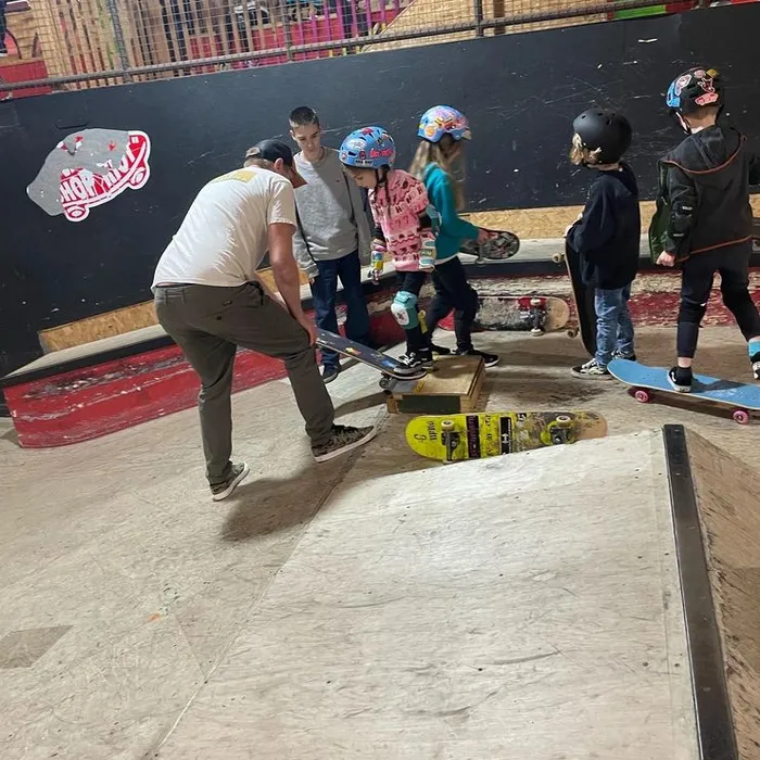 Coach Rich crouched on a ramp helping a young skater while the rest of the group watches