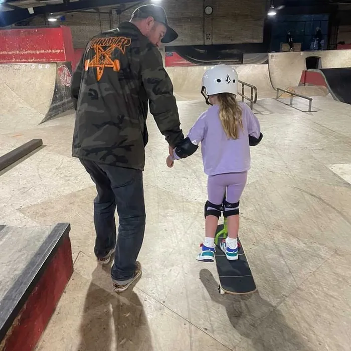 Coach Rich holding a young girl's hand as she stands on her skateboard at Prevail Skatehouse