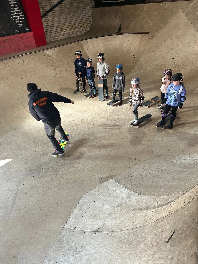 Coach Pye dropping in while kids watch from the lip of the bowl at Prevail Skatehouse