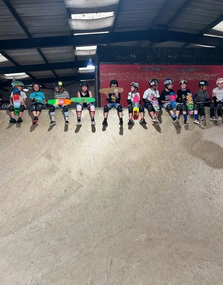 A row of kids in helmets and pads sitting at the top of the ramp at Prevail Skatehouse