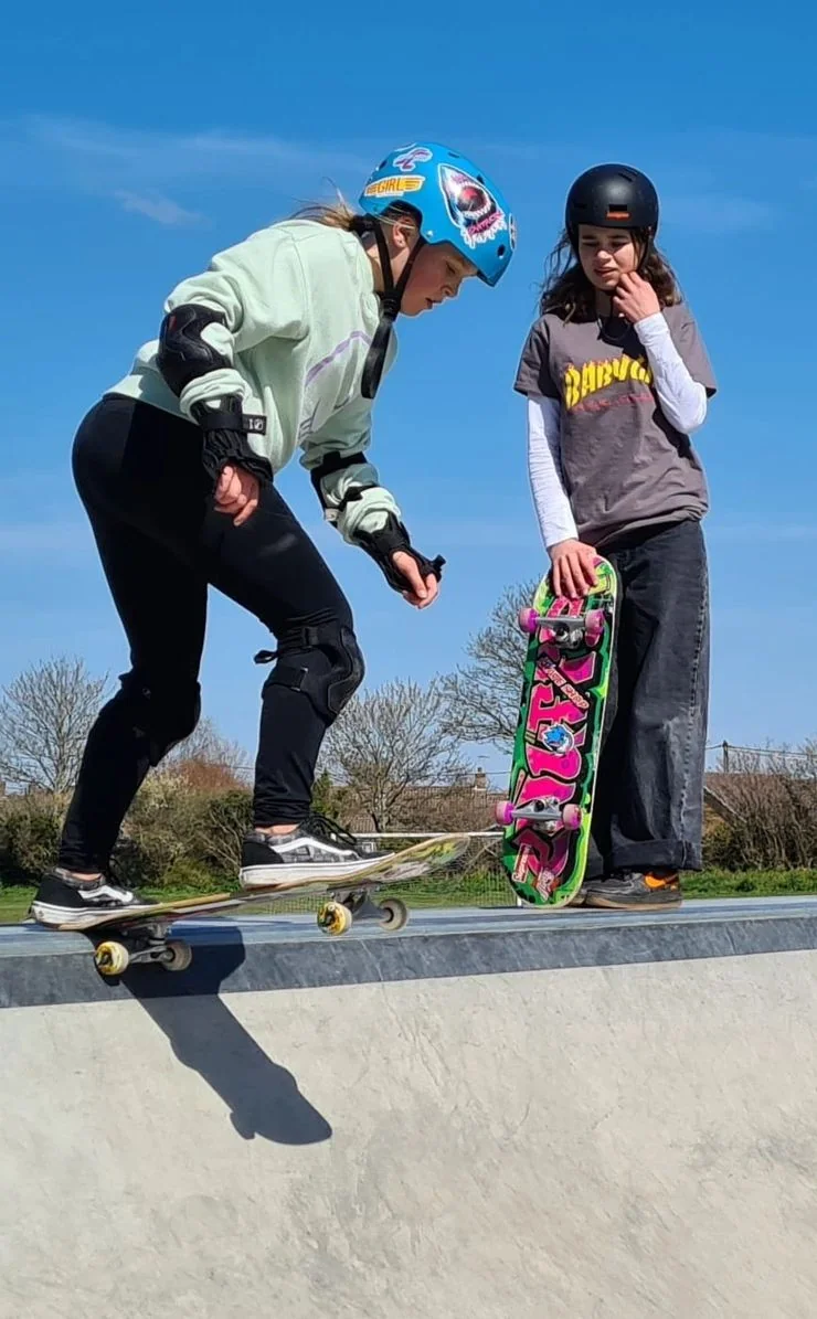 Two young skaters at the edge of the bowl at a Dorset skatepark on a sunny day