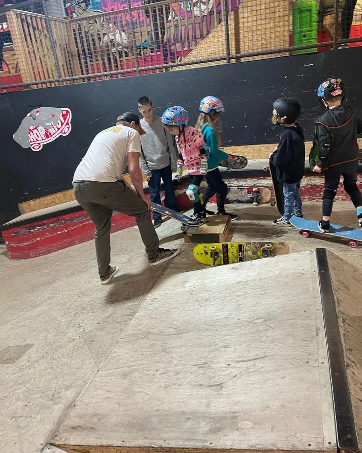 Coach Rich crouched on a ramp helping a young skater while the rest of the group watches